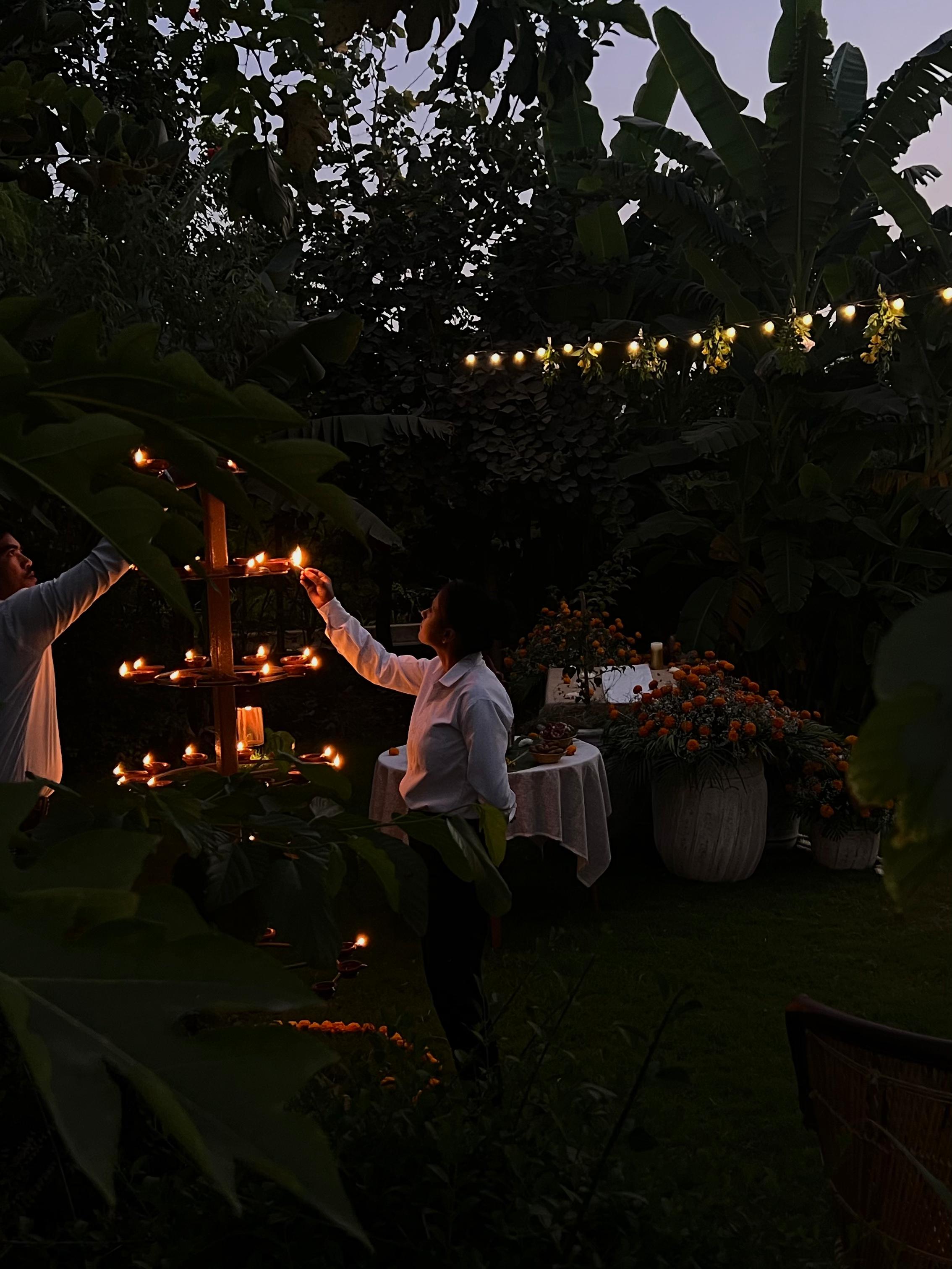 Staff lighting diyas under string lights at dusk